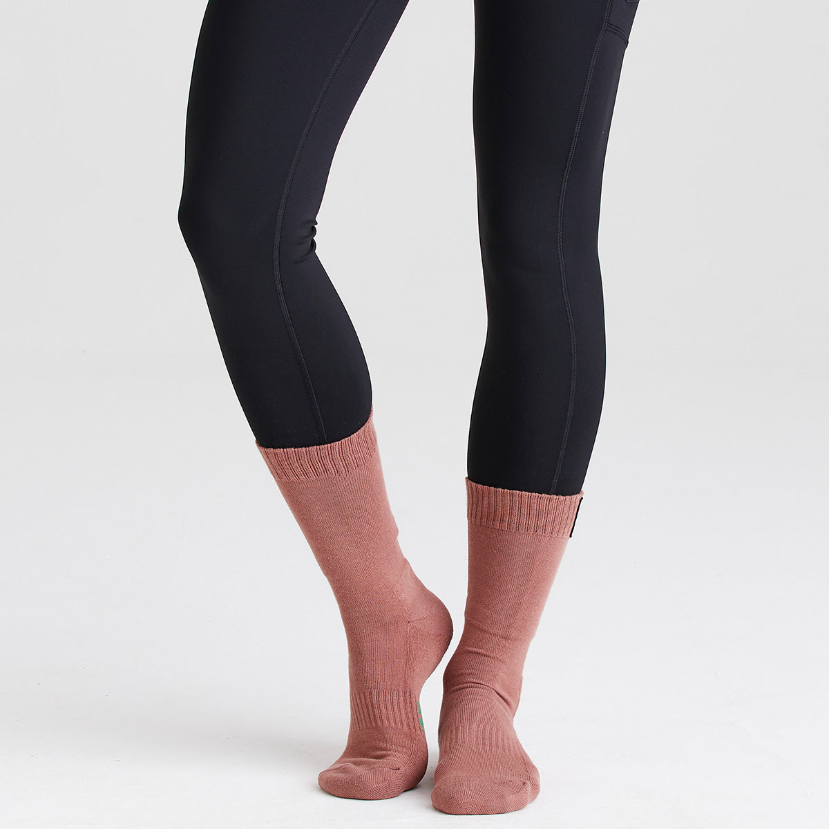 Dusty pink ribbed mid-length socks worn with black leggings, rear view on a grey background