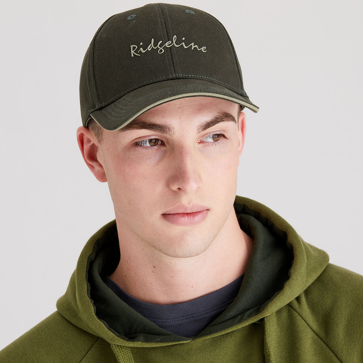 Man wearing a green cap with 'Ridgeline' branding and a matching green hoodie on a light gray background.