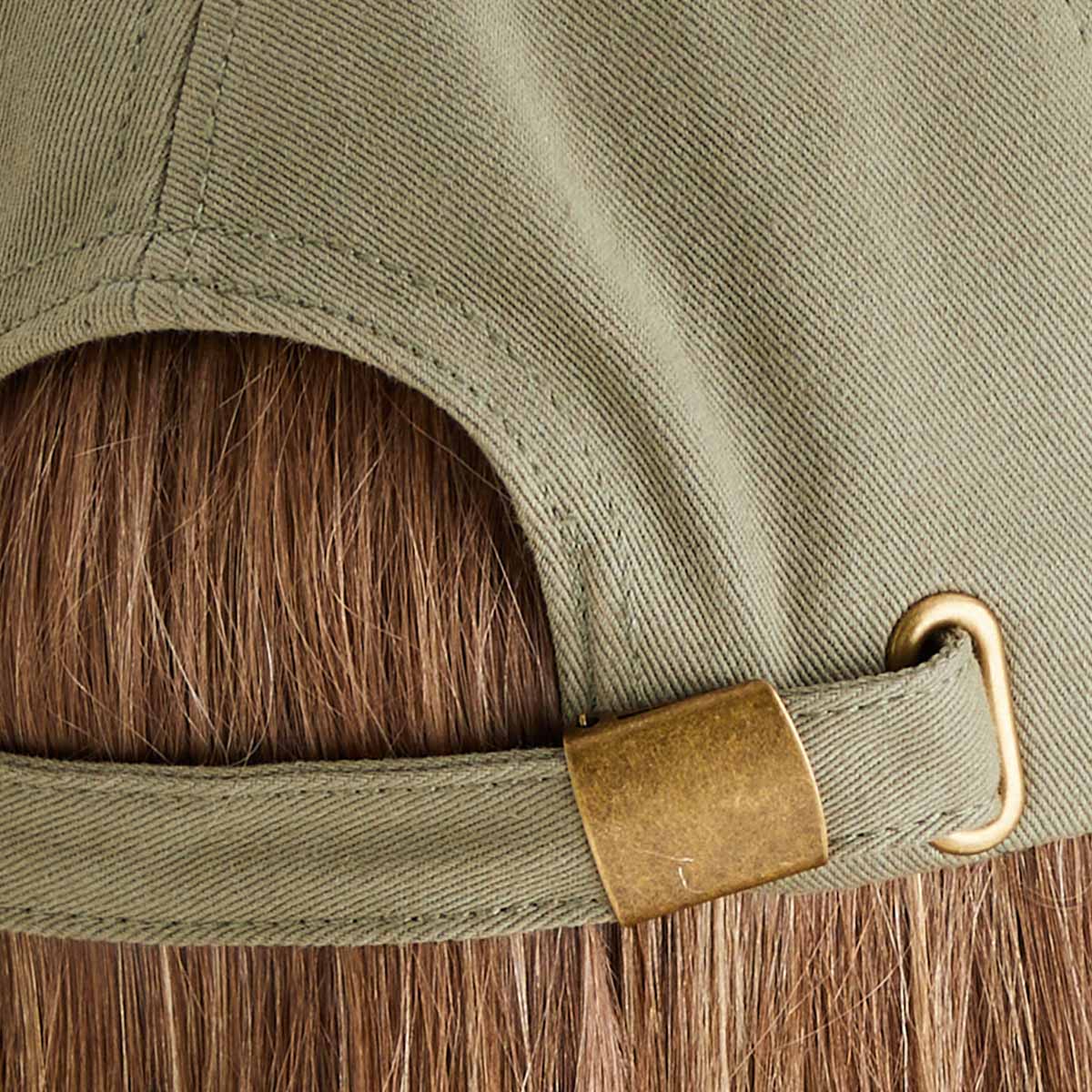 Close-up of a green cap with a brown brim and gold buckle on a wooden surface.