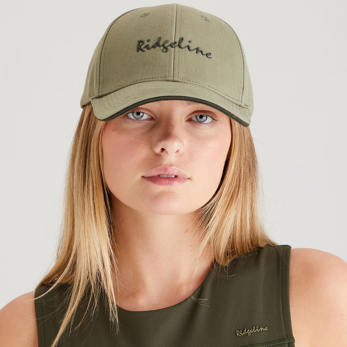 Woman wearing an olive green cap and tank top with 'Ridgeline' branding on a light gray background