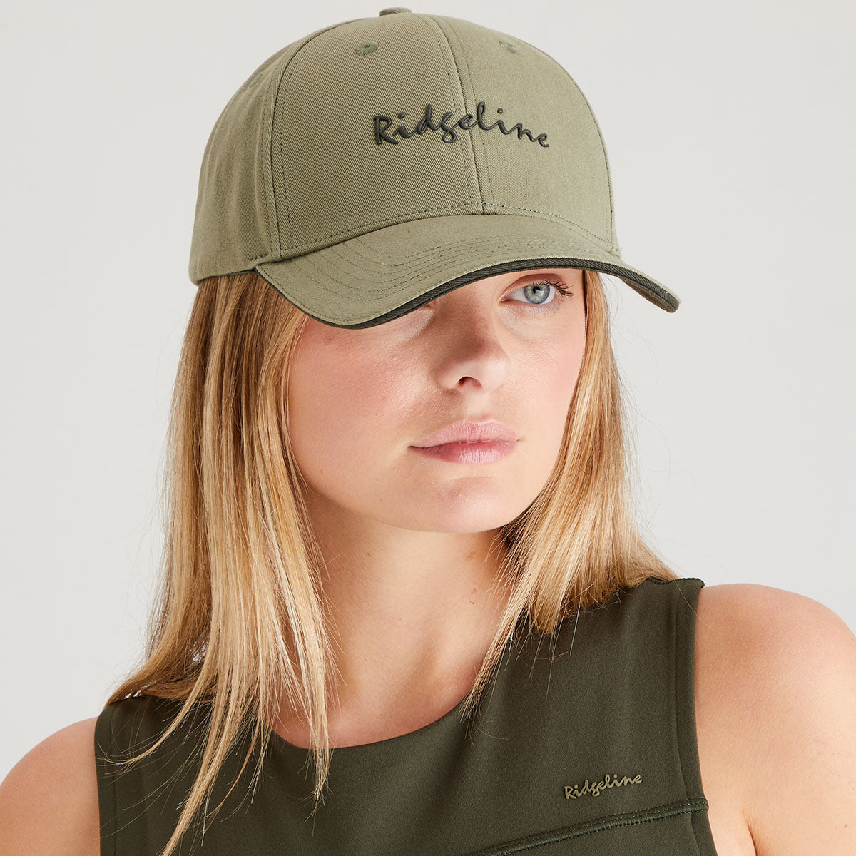 Woman wearing a green cap and sleeveless top with 'Ridgeline' branding on a light gray background