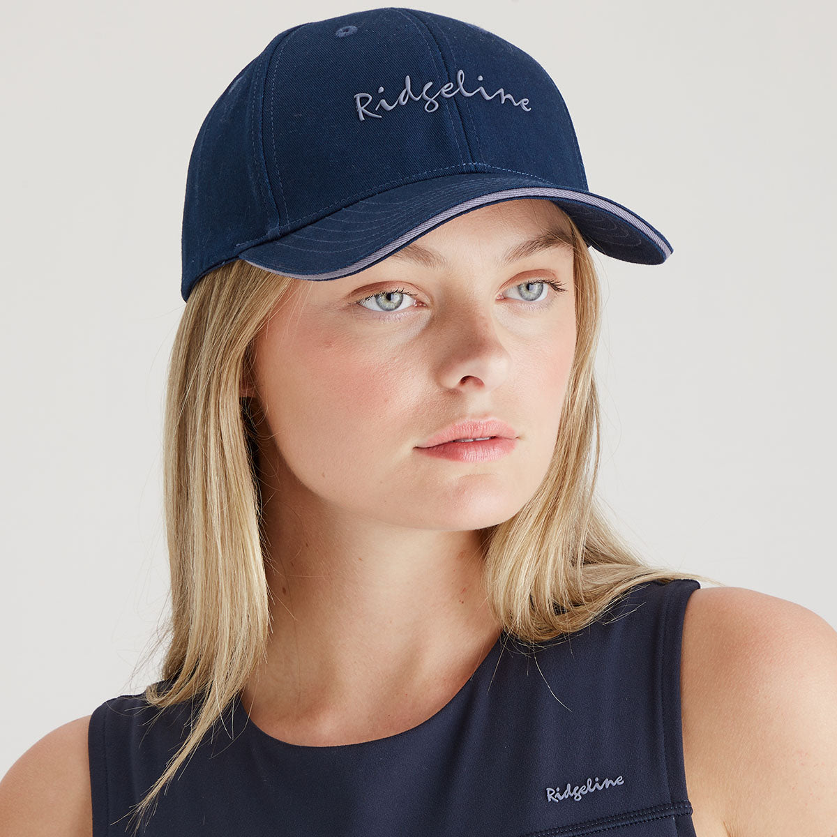 Woman wearing a navy cap and tank top with 'Ridgeline' branding on a light gray background