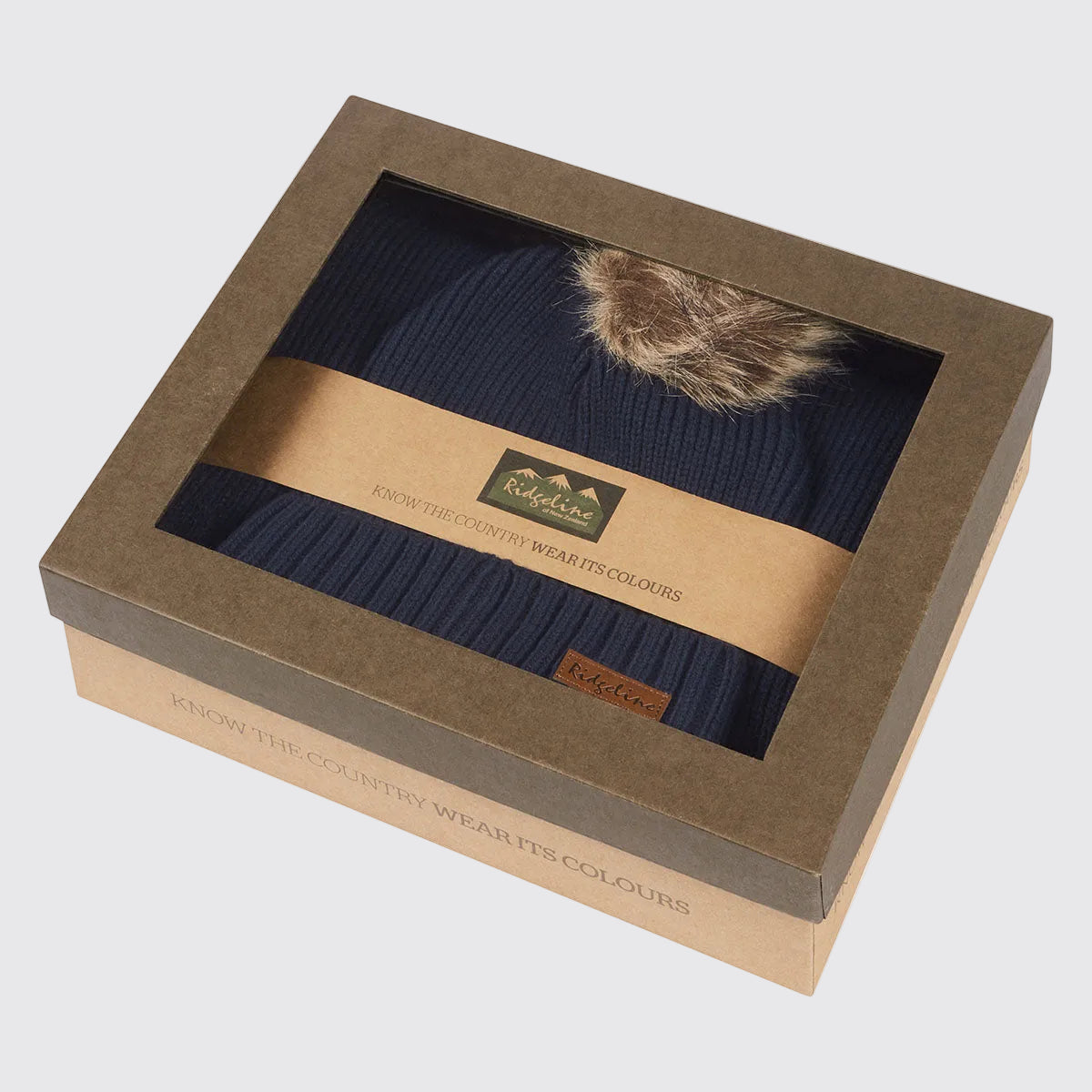 Navy ribbed knit beanie hat with faux fur pom pom in windowed gift box, angled view.