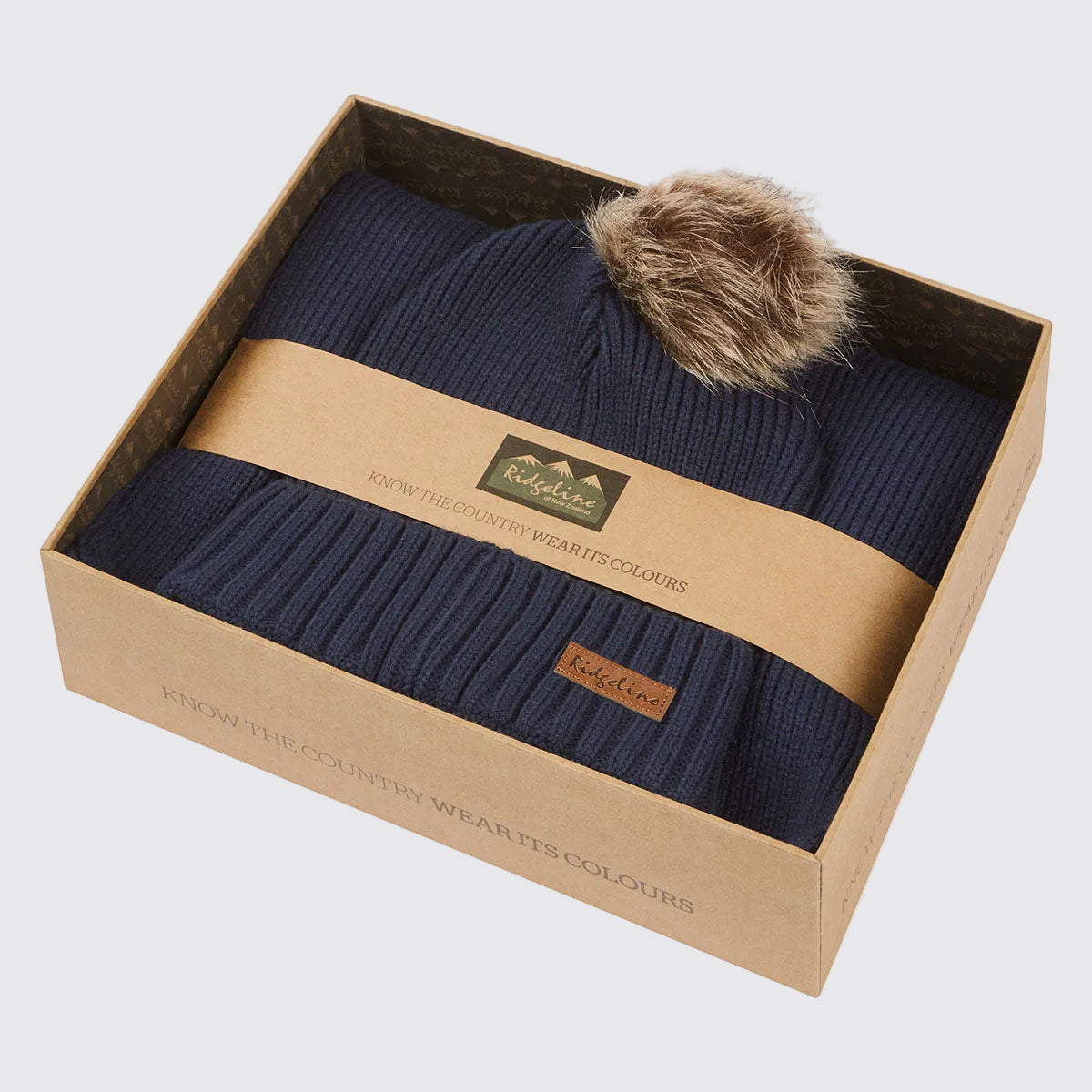 Navy ribbed knit beanie hat with faux fur pom pom in branded gift box, angled view.