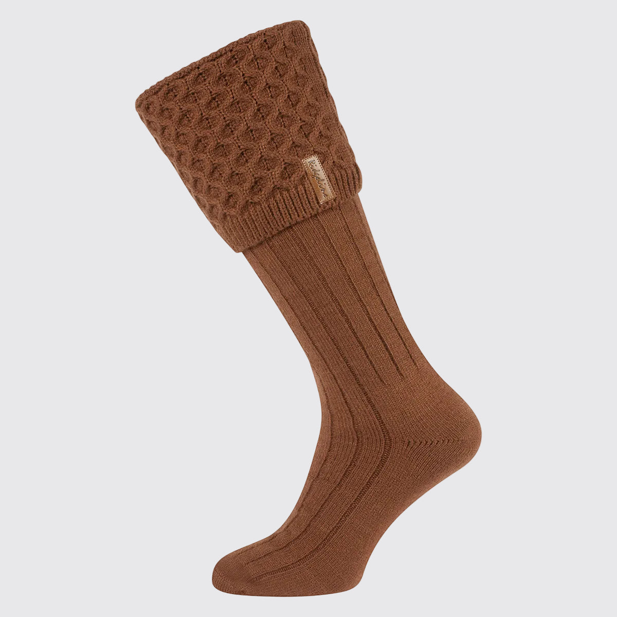 Single rust-brown welly sock with a long ribbed leg and a chunky cable-knit turnover cuff, displayed against a light grey background. The cuff features a textured cable-knit pattern and a small Ridgeline branded tag on the side. Designed to be worn with wellington boots, the sock combines classic country styling with added warmth, comfort, and insulation for cold-weather outdoor wear.
