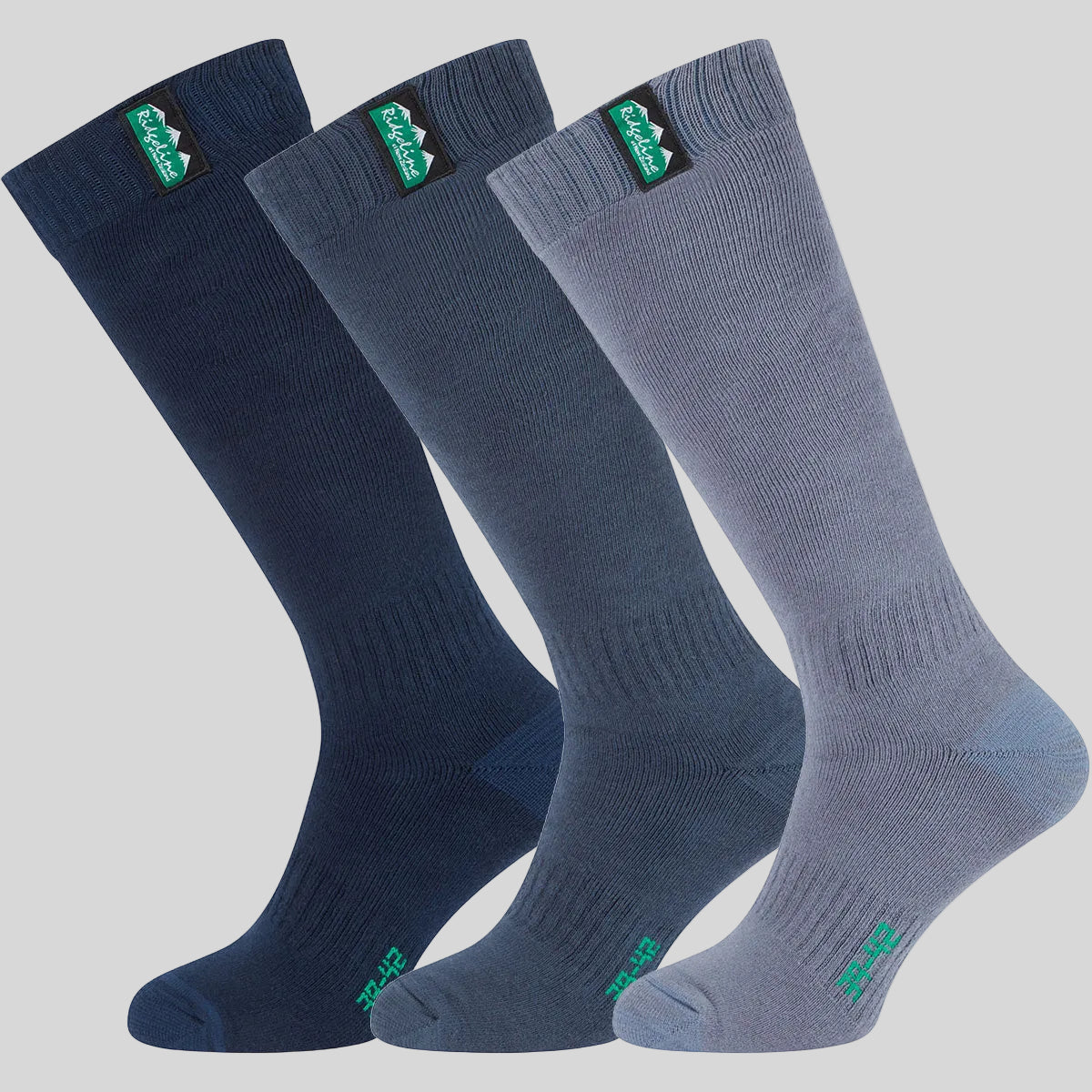 Three pairs of full-calf socks in navy, dark blue, and storm blue, arranged diagonally on a grey background. Each pair features a green and black logo patch near the cuff.