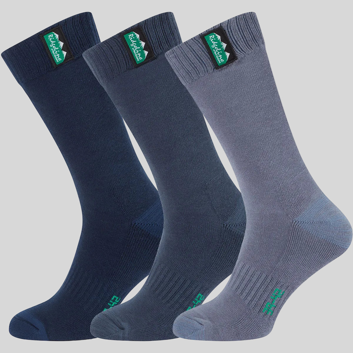Three pairs of mid-calf socks in navy, slate blue, and storm blue, arranged in a fan shape against a plain grey background. Each sock features a green and black logo patch on the cuff.