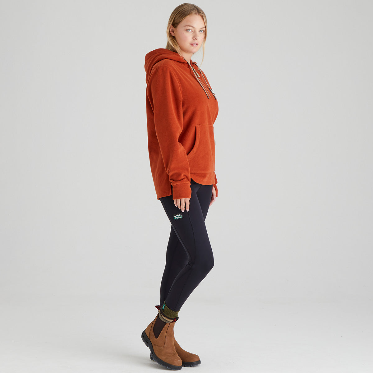 Person wearing an orange hoodie, black leggings, and brown boots on a light grey background