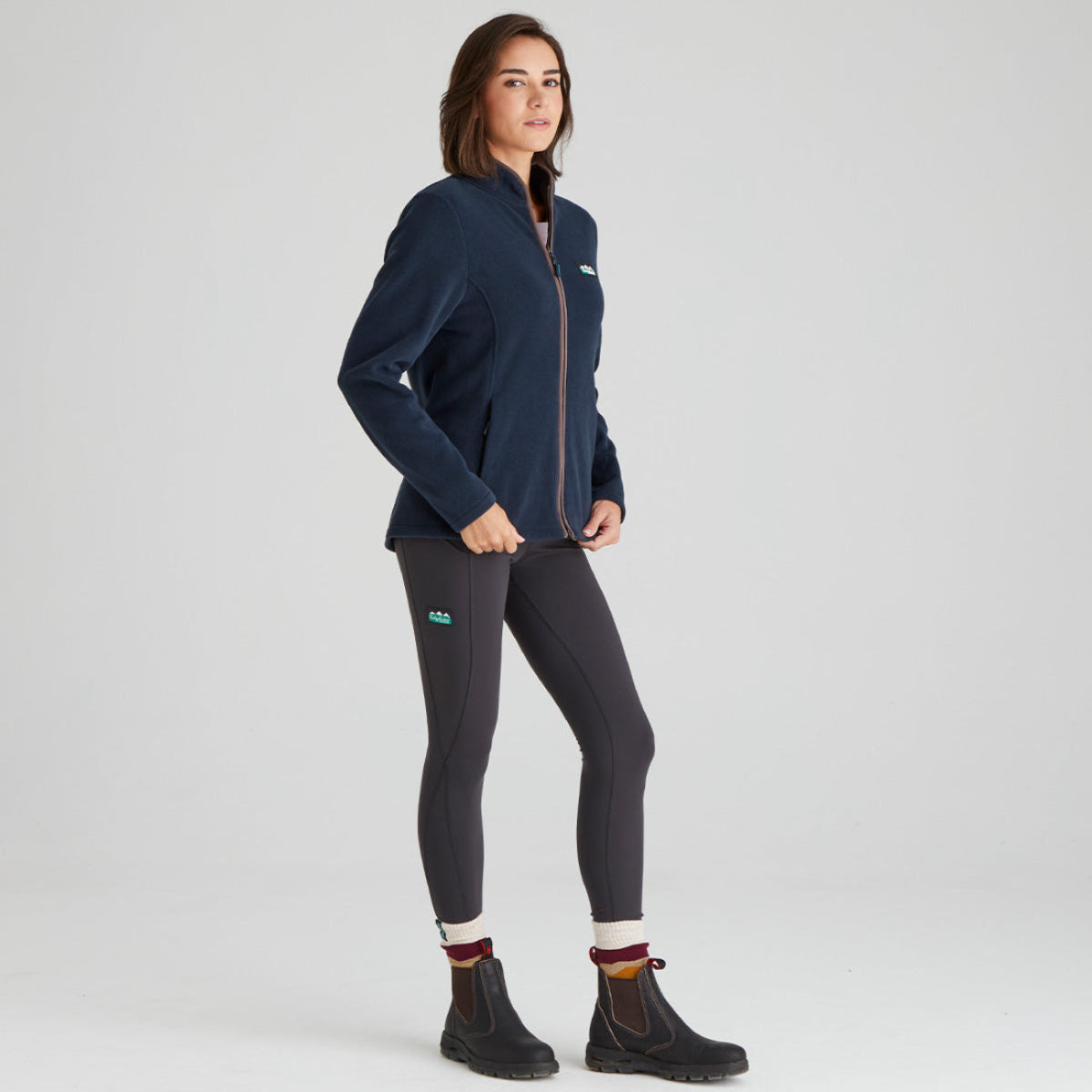 Woman wearing a navy fleece jacket and dark leggings on a light grey background