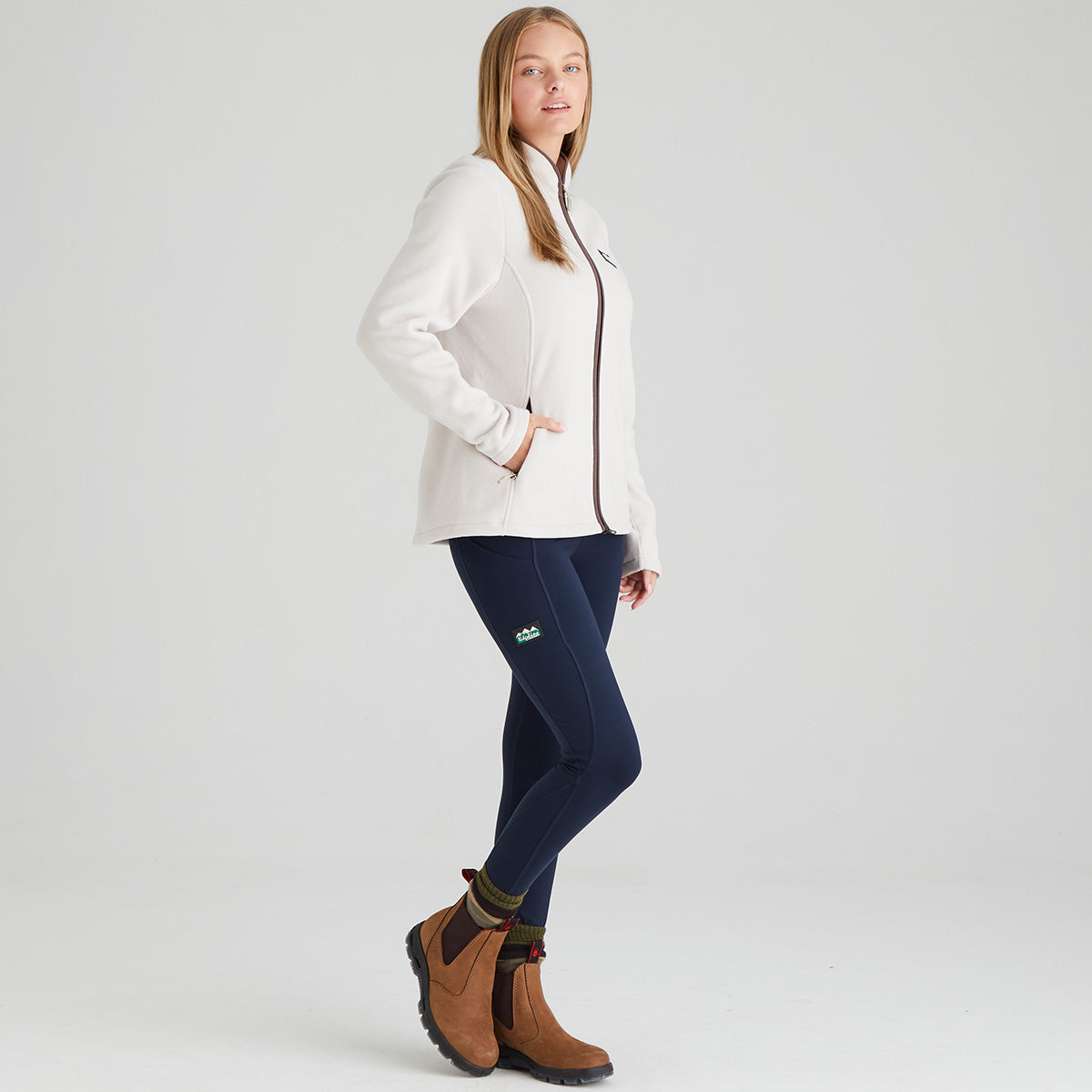 Person wearing a white full zip fleece jacket, navy leggings, and brown boots on a light grey background
