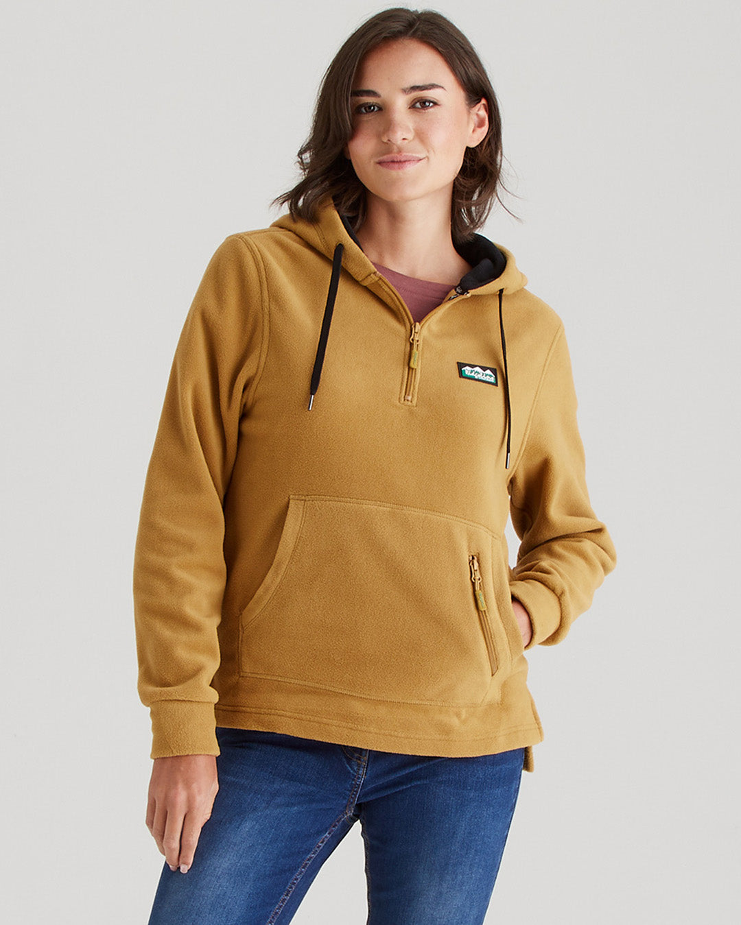 Woman wearing a mustard yellow hoodie with a brand logo on a light gray background