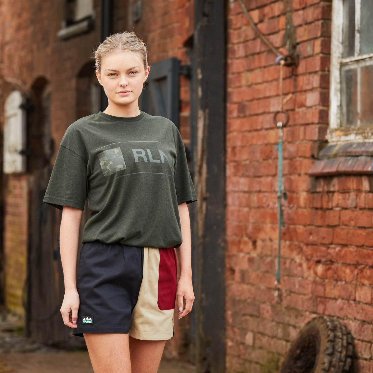 Person wearing a green t-shirt with 'RLNZ' logo in front of a brick wall.