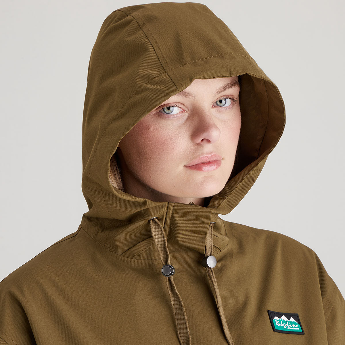 Person wearing a brown hooded jacket with a visible brand logo on a plain background