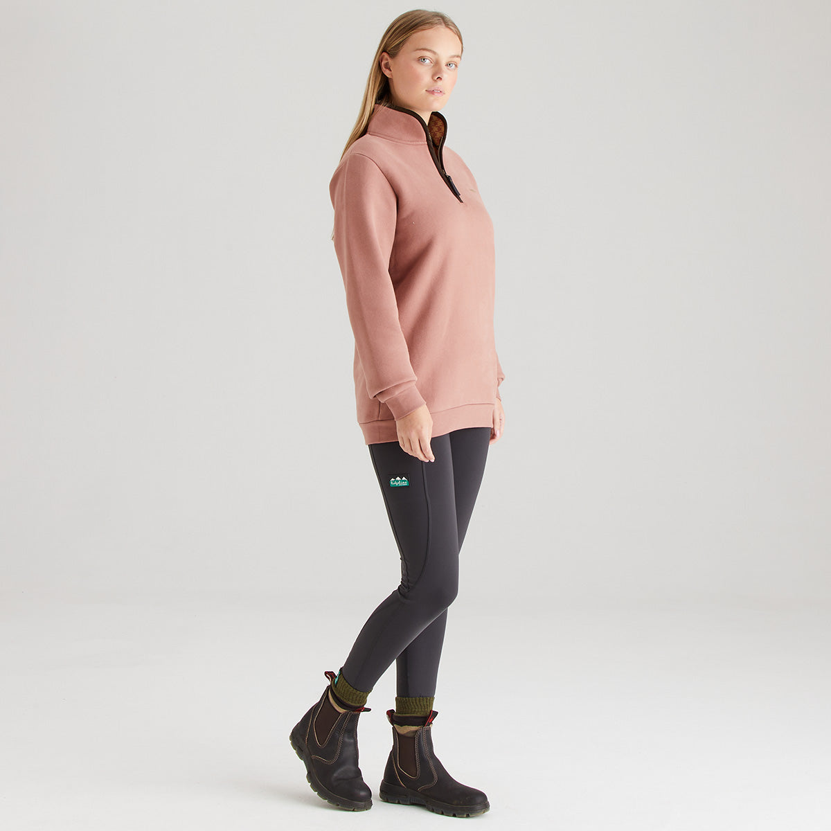 Person wearing a pink pullover and dark leggings on a white background