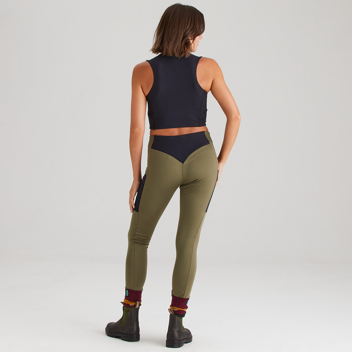 Person wearing a black sleeveless top and olive green leggings on a light gray background