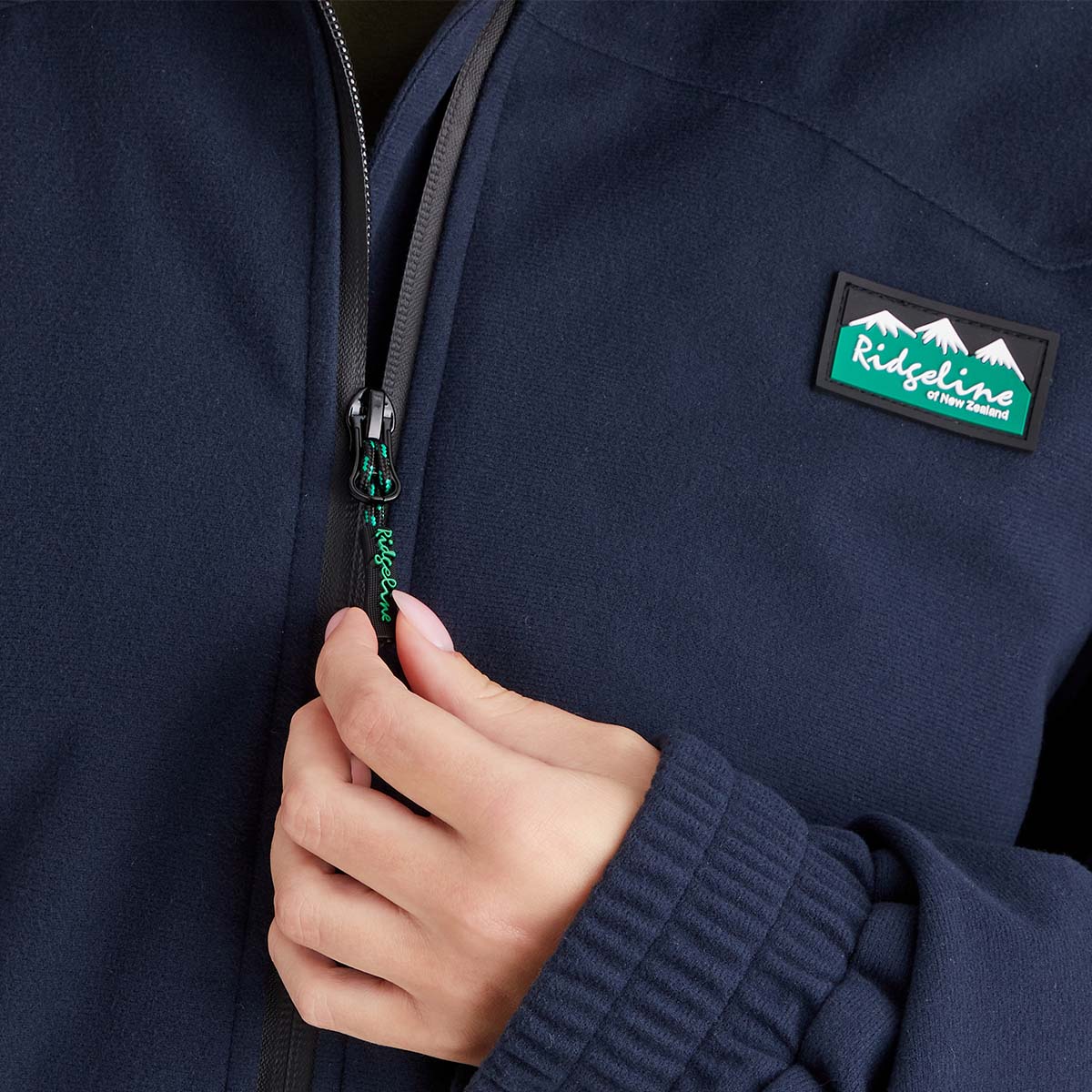 Navy blue jacket with a brand logo on the chest, held by a hand.