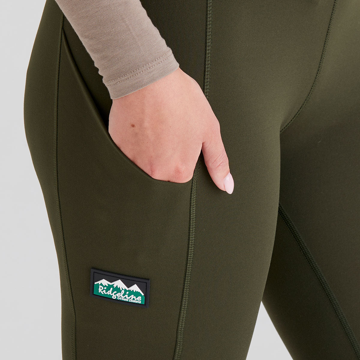 Close up of pocket on green leggings with a visible ridgeline clothing brand logo on a plain background