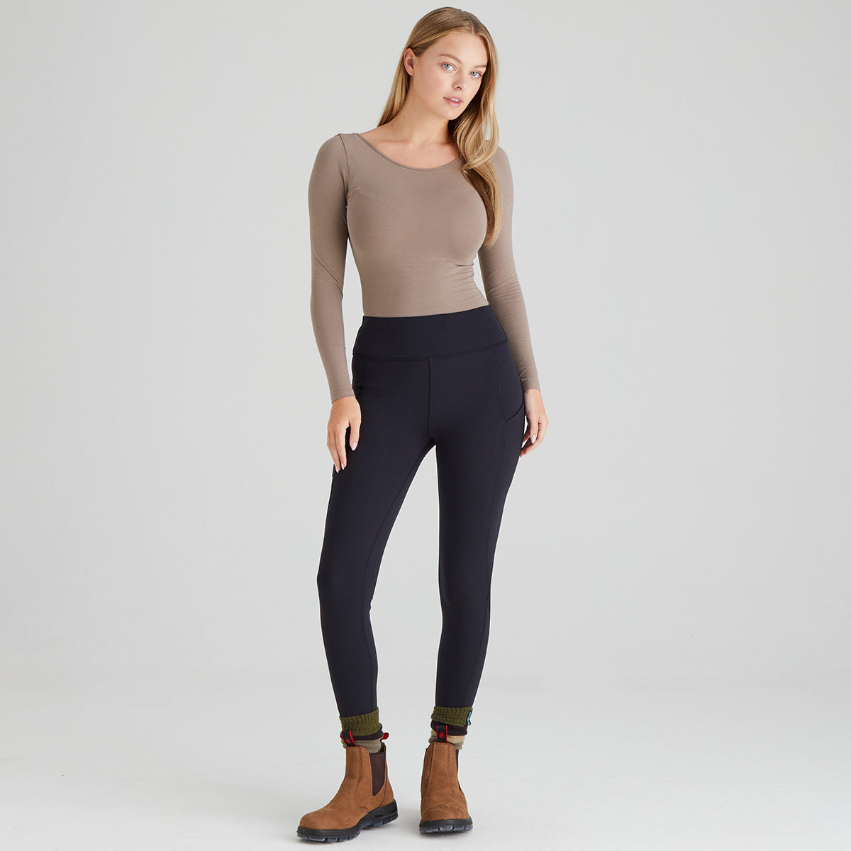 Woman wearing a brown long-sleeve top and black leggings on a white background