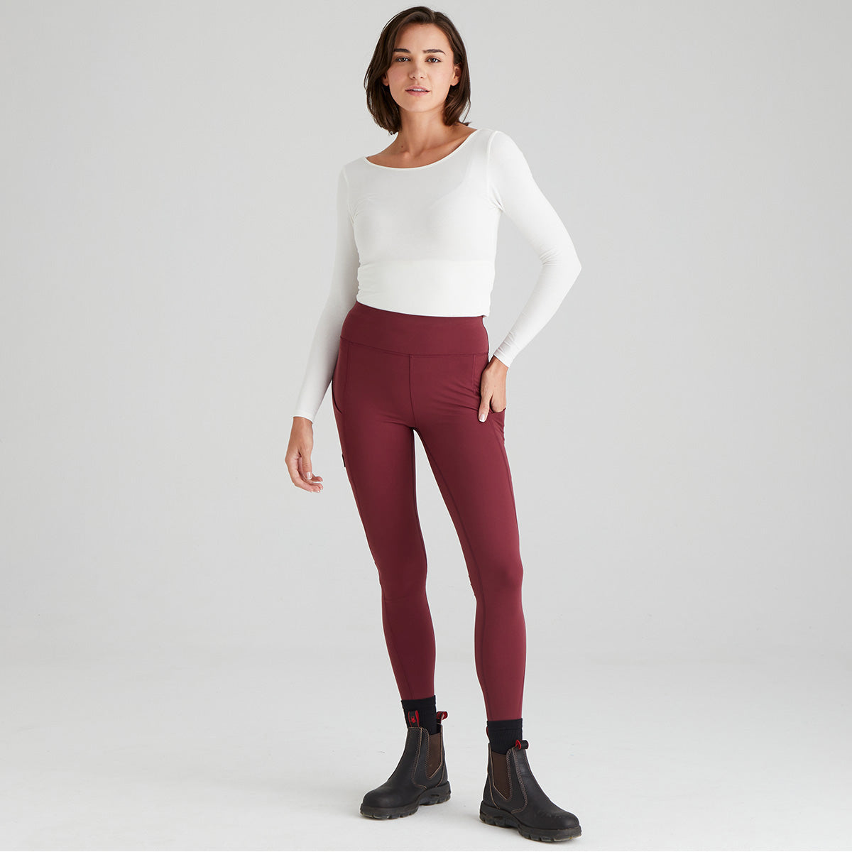 Woman wearing a white top and maroon leggings on a light gray background