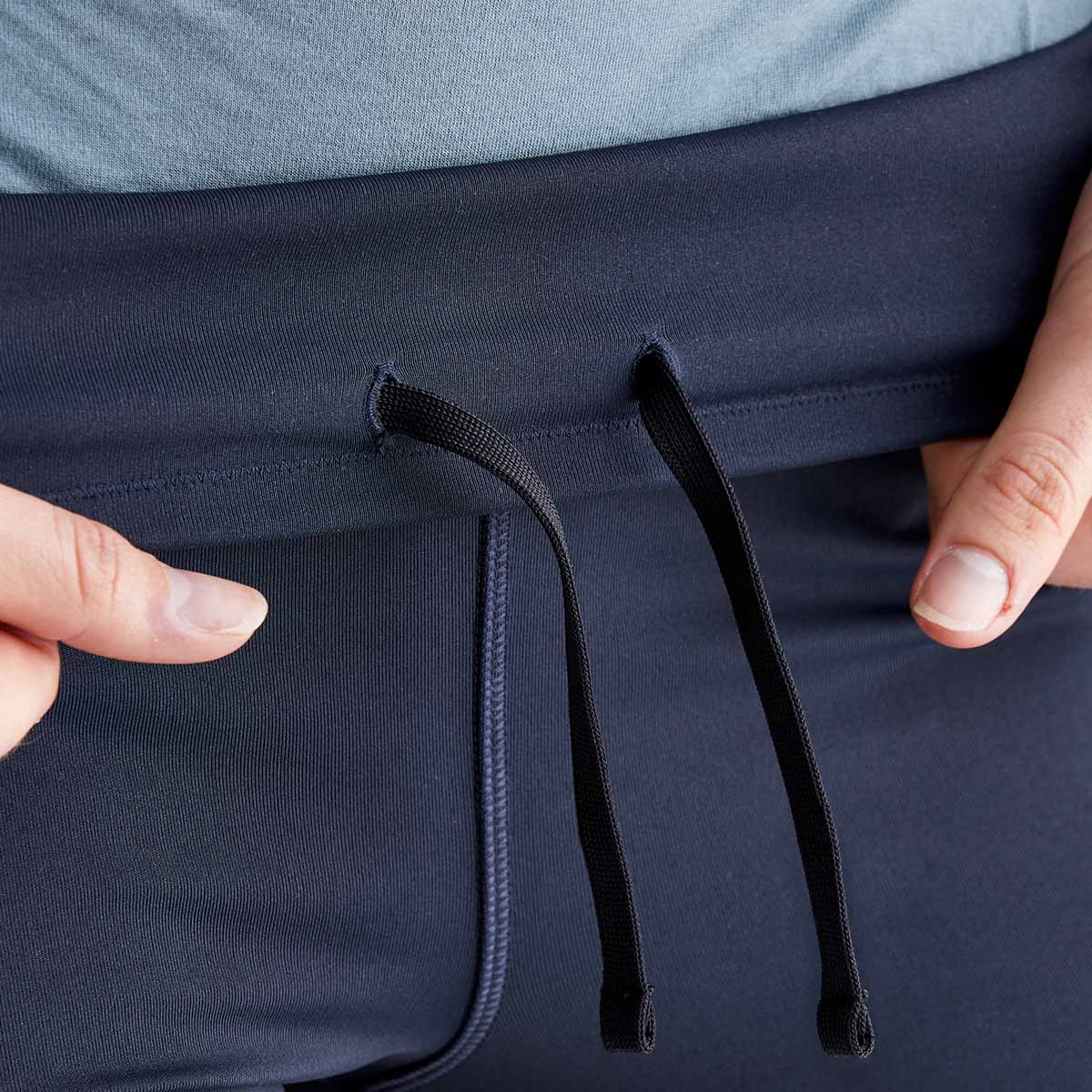 Close-up detail of Ridgeline infinity pro navy performance leggings showing the high-rise waistband with an adjustable internal drawcord for a secure fit. The smooth stretch fabric and supportive waistband construction are highlighted, while hands gently pull the waistband to demonstrate flexibility and comfort. Photographed against a plain light grey studio background, the image showcases the leggings' functional fit and performance-focused design.
