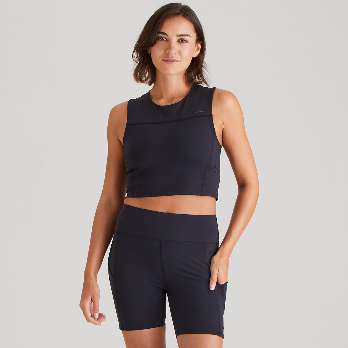 Woman wearing a black sleeveless top and shorts on a gray background