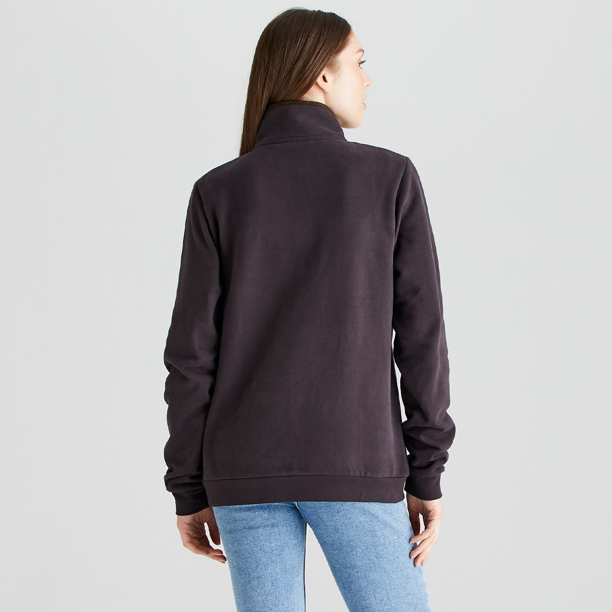 Back view of a person standing against a light gray studio background, wearing a dark brown quarter-zip sweatshirt and light blue jeans. The sweatshirt has a high collar, long sleeves, and ribbed cuffs and hem. The garment is shown from the rear to highlight the fit, length, and plain back design. Lighting is even and neutral, providing a clear view of the fabric and silhouette.
