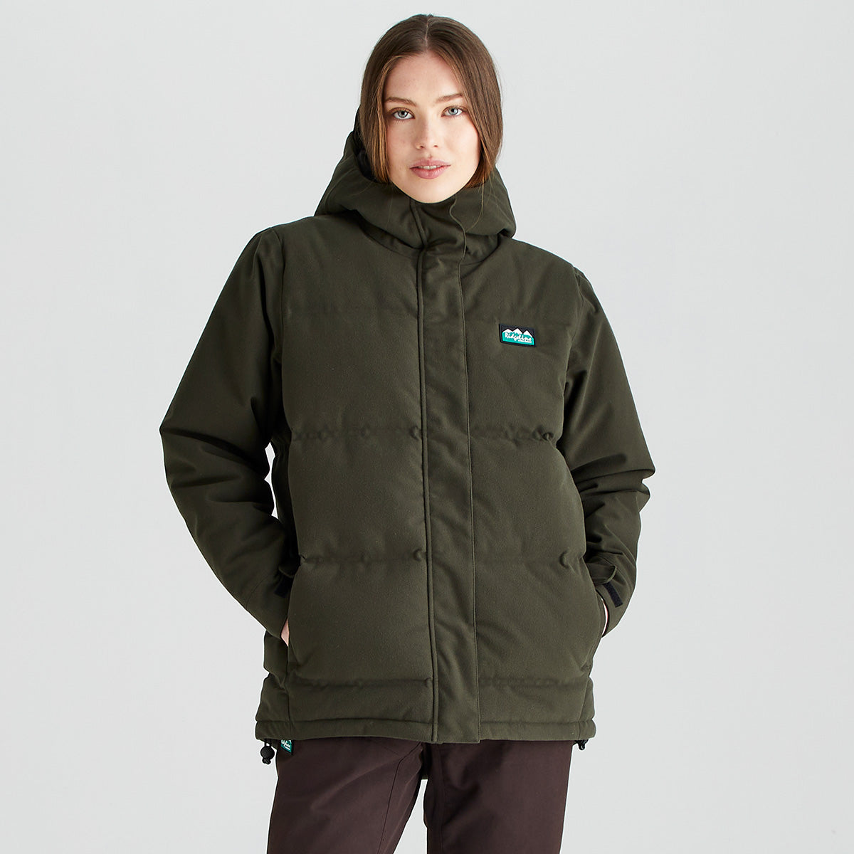 Person wearing a Ridgeline insulated hooded jacket in olive green with a full-length front zip, high collar, padded construction and side pockets, shown against a light grey studio background.
