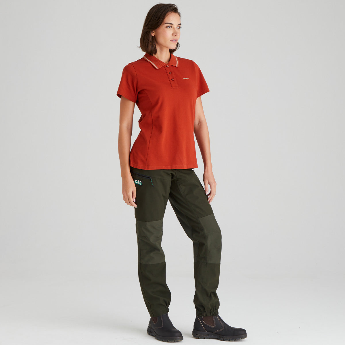 woman wearing a orange polo shirt and green pants on a light grey background