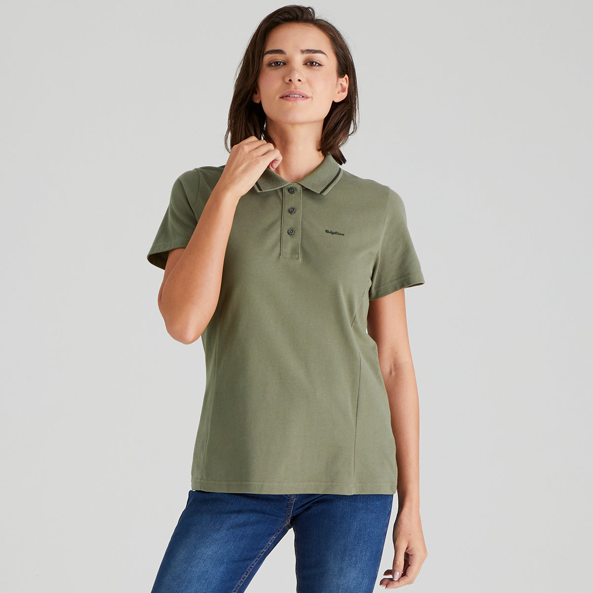 Woman wearing a green polo shirt and blue jeans on a grey background