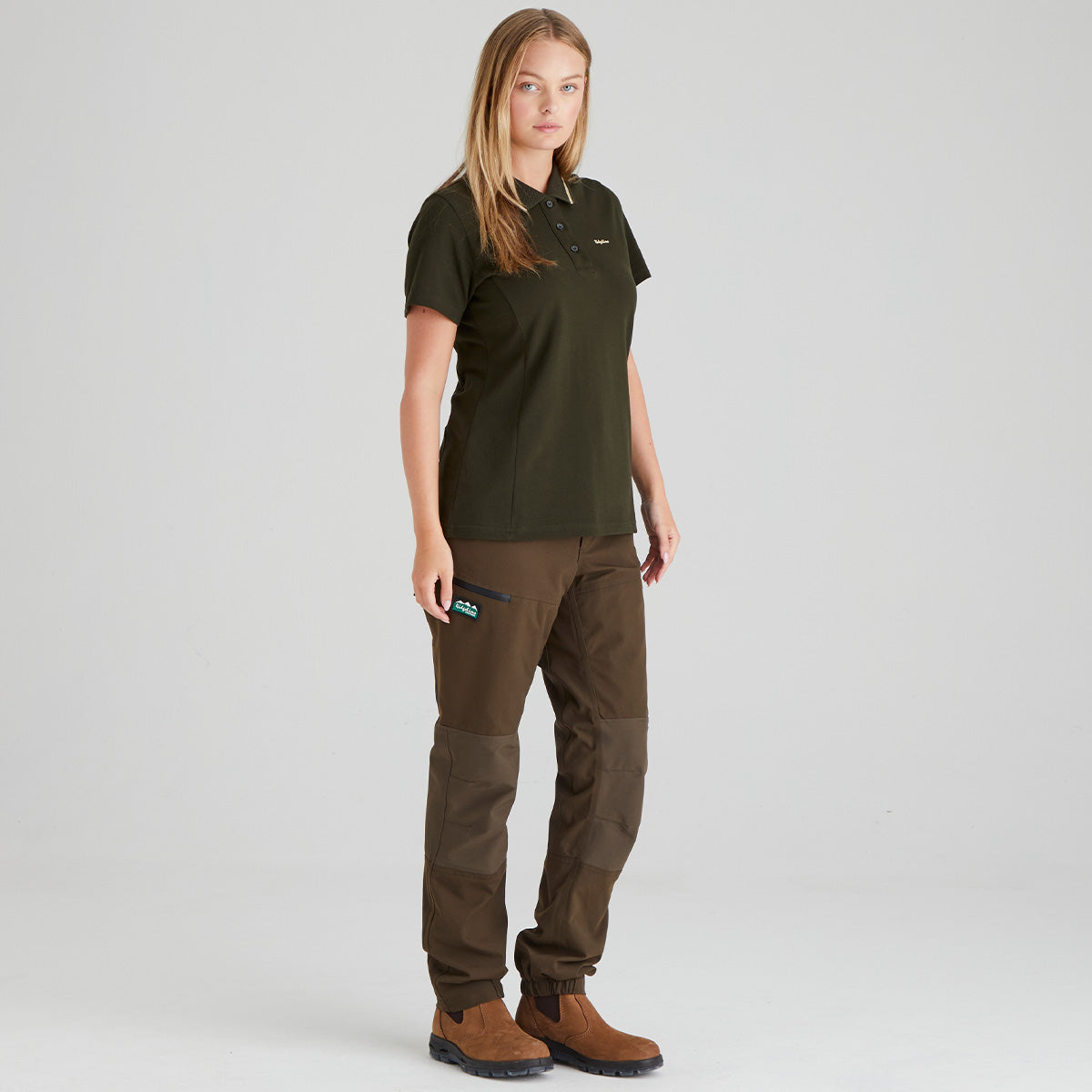 Woman wearing a green shirt and brown pants on a light gray background