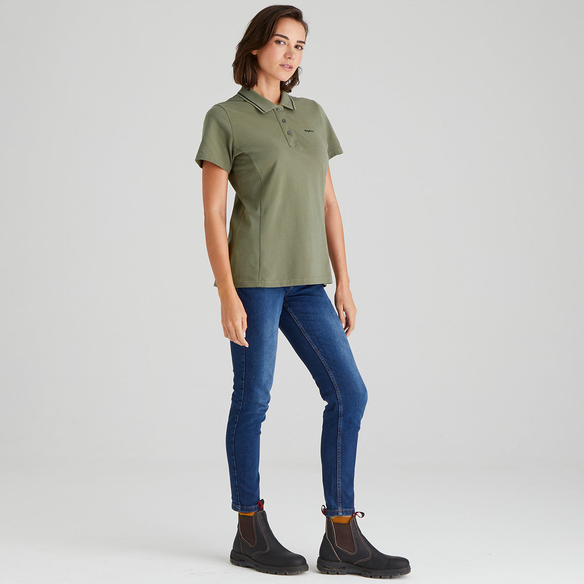 Woman wearing a green polo shirt and blue jeans on a light gray background