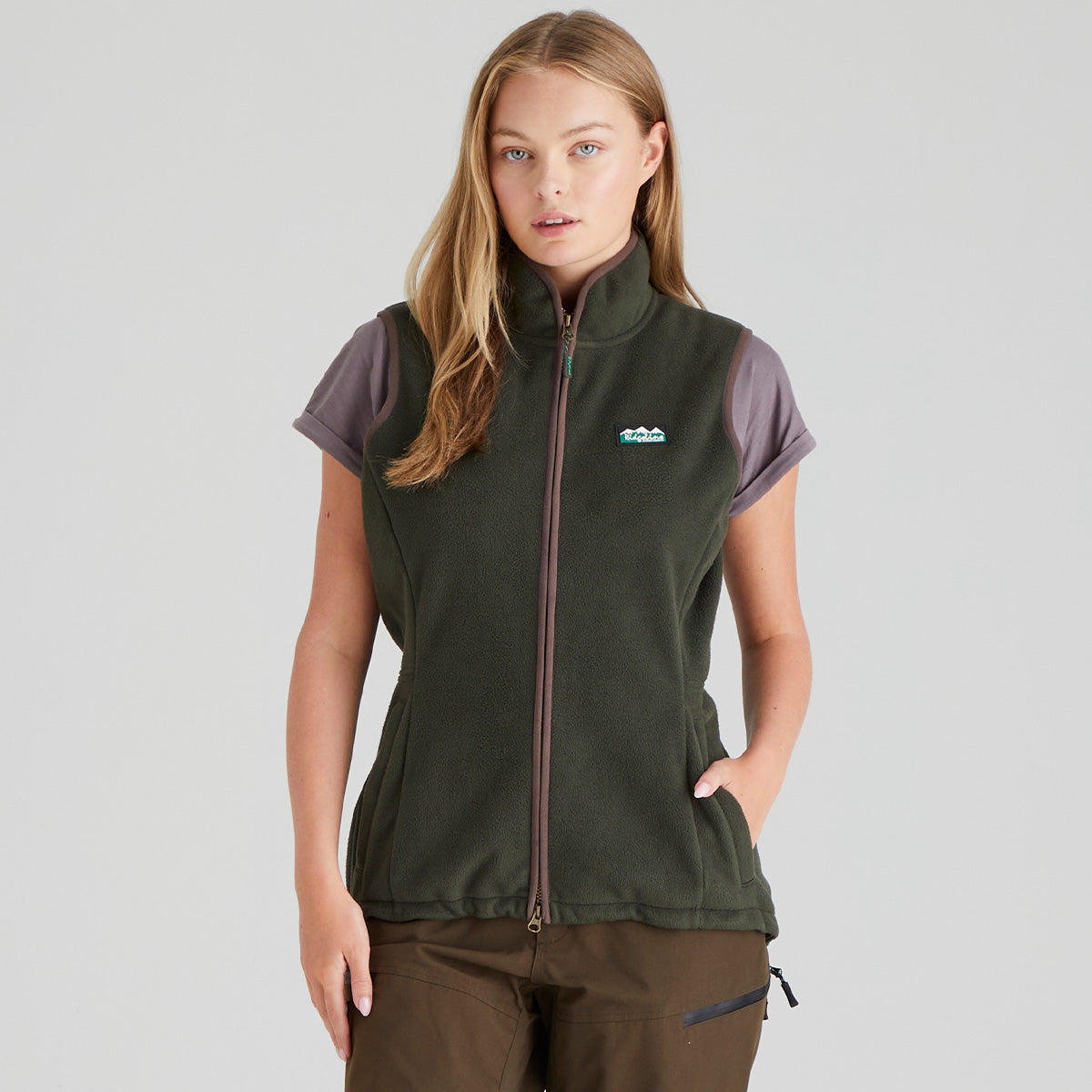 Woman wearing a green fleece gilet jacket with a Ridgeline Clothing brand logo on a grey background