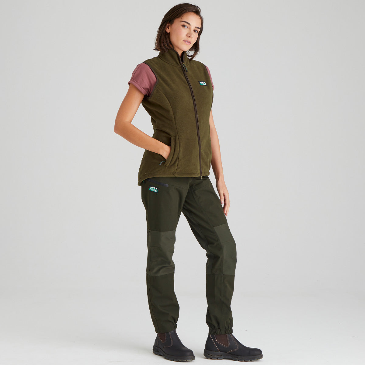 Woman wearing a brown fleece gilet and pants on a light grey background
