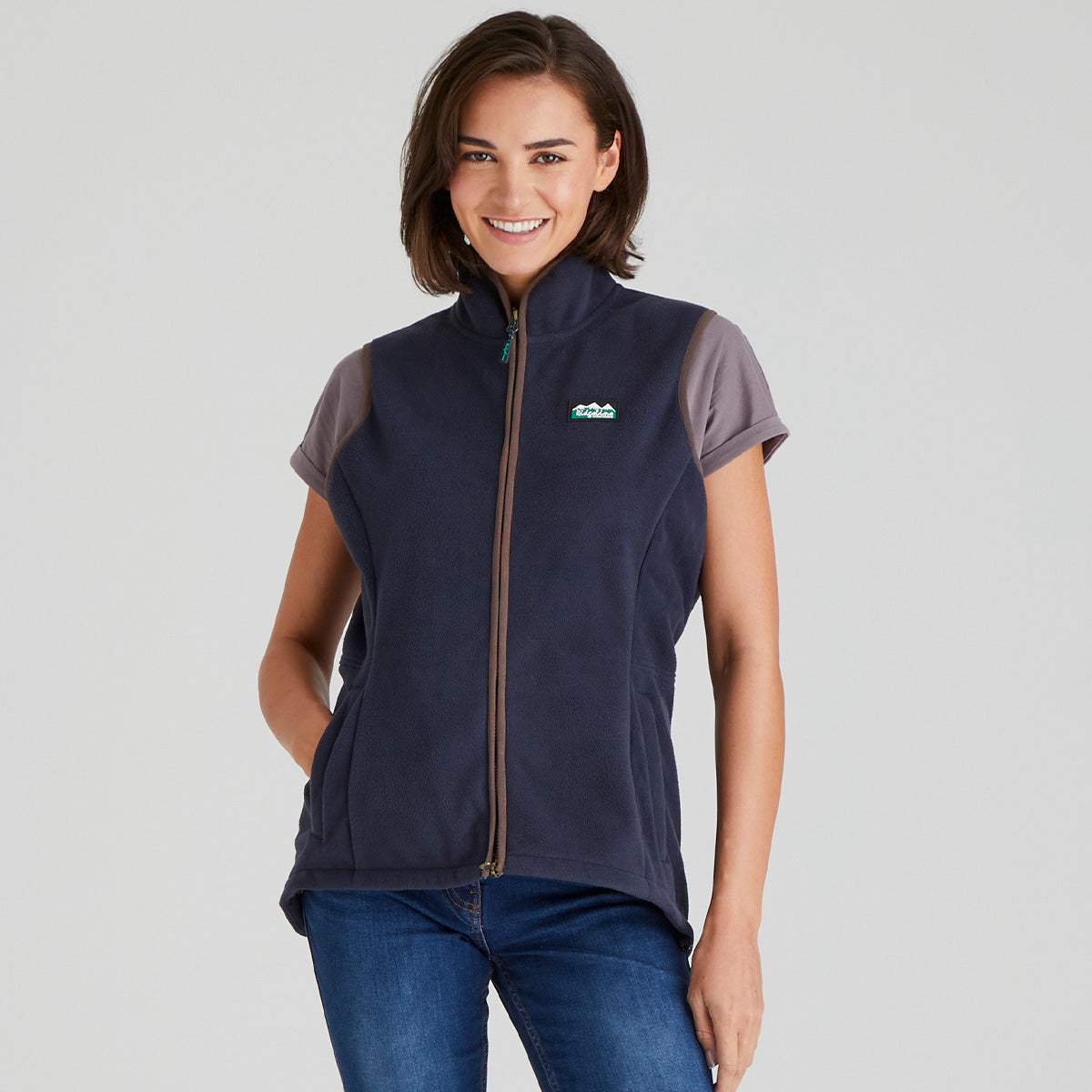 Woman wearing a navy fleece gilet vest with a ridgeline clothing logo on a grey background