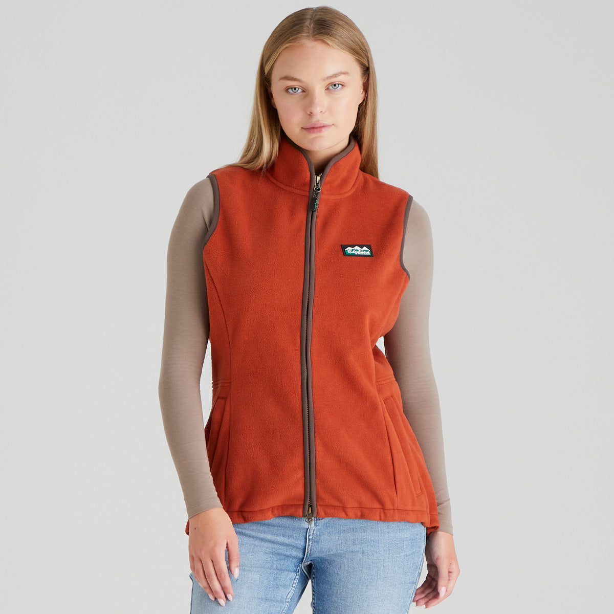 woman wearing an orange fleece gilet  vest with a ridgeline clothing brand logo on a grey background