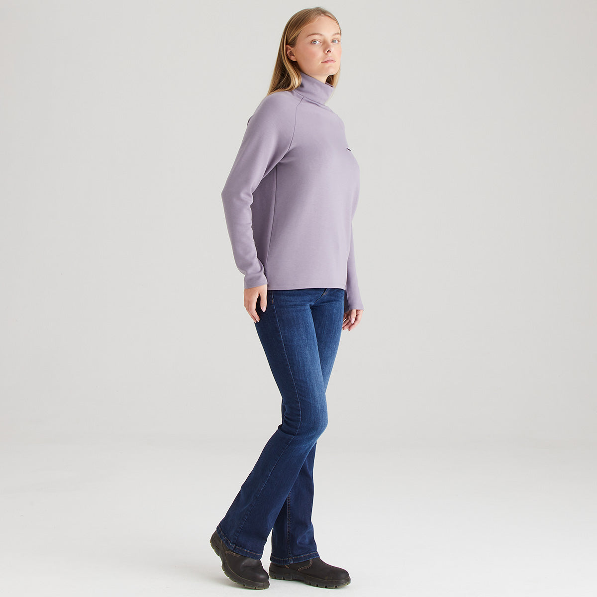 Person wearing a light purple turtleneck and blue jeans on a white background