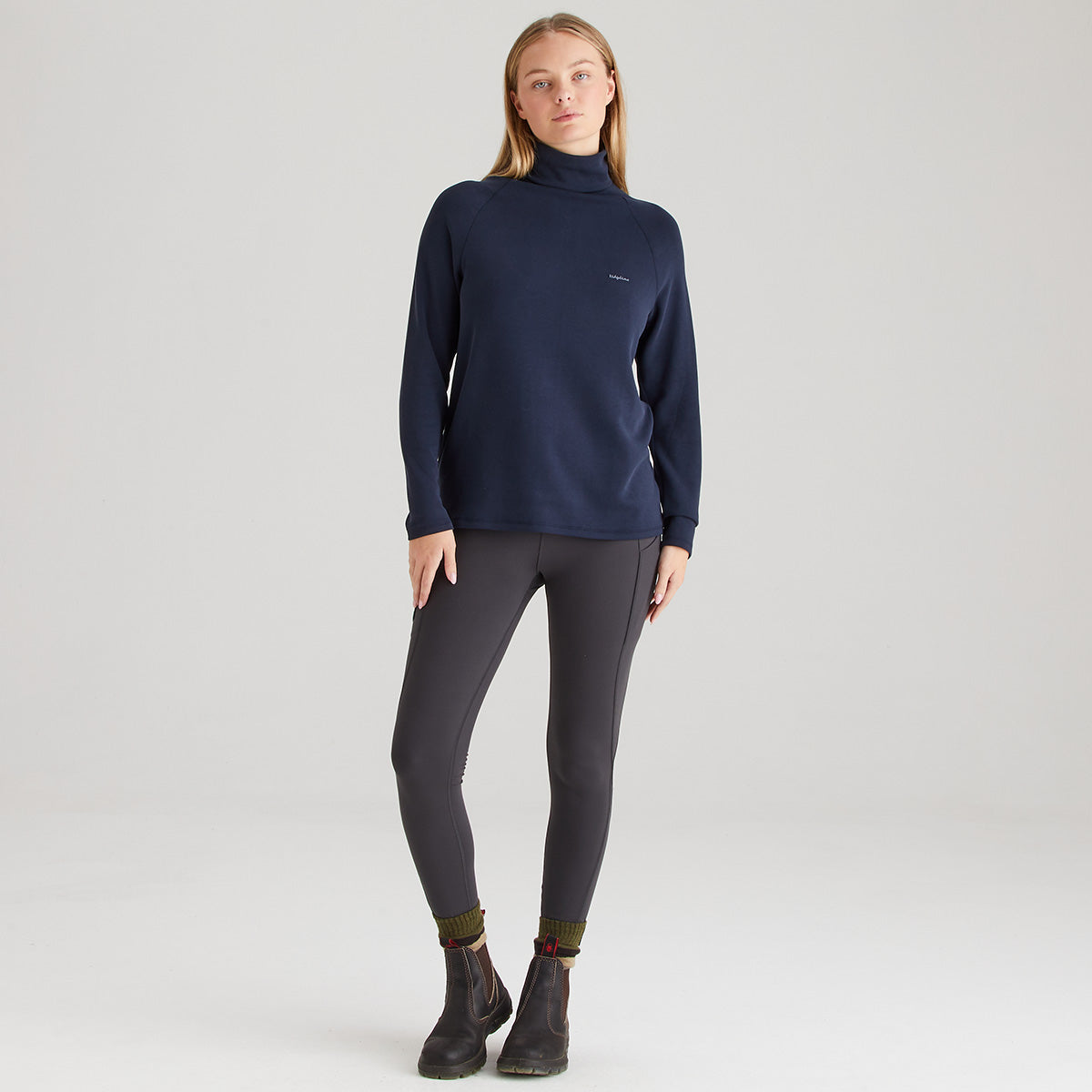 Woman wearing a navy blue turtleneck sweater and gray leggings on a white background