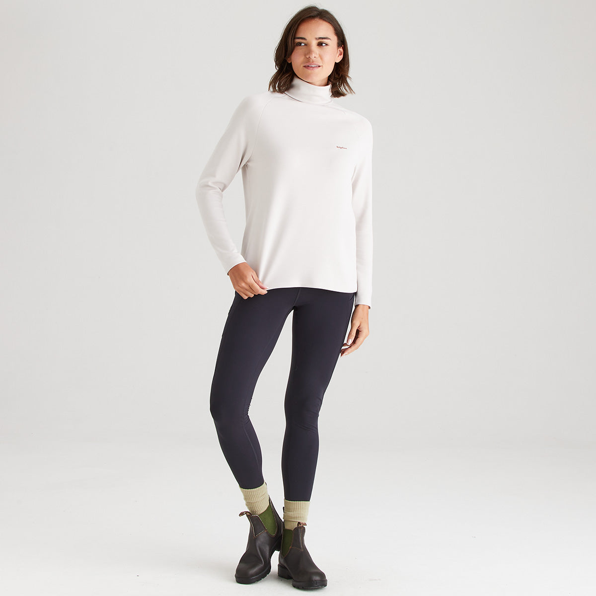 Woman wearing a white turtleneck sweater and dark leggings on a light gray background