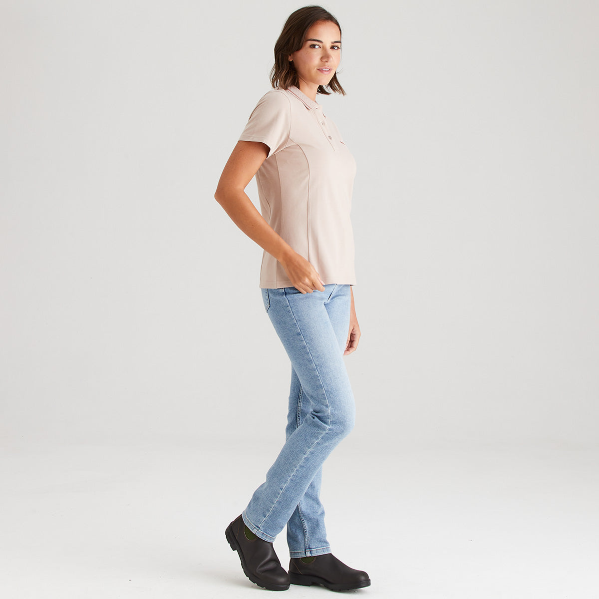Woman wearing a blush polo and light blue jeans on a white background