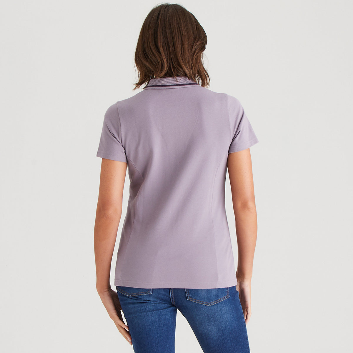 Person wearing a light purple polo shirt and blue jeans on a white background