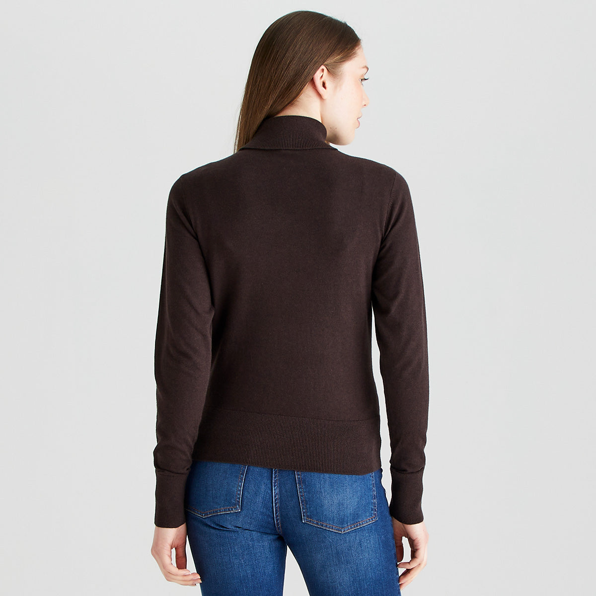 Rear view of a Ridgeline dark brown knitted roll neck jumper, showing the high folded turtleneck, long sleeves, and ribbed hem and cuffs. The fine-knit sweater is worn with blue jeans and photographed against a light grey studio background.
