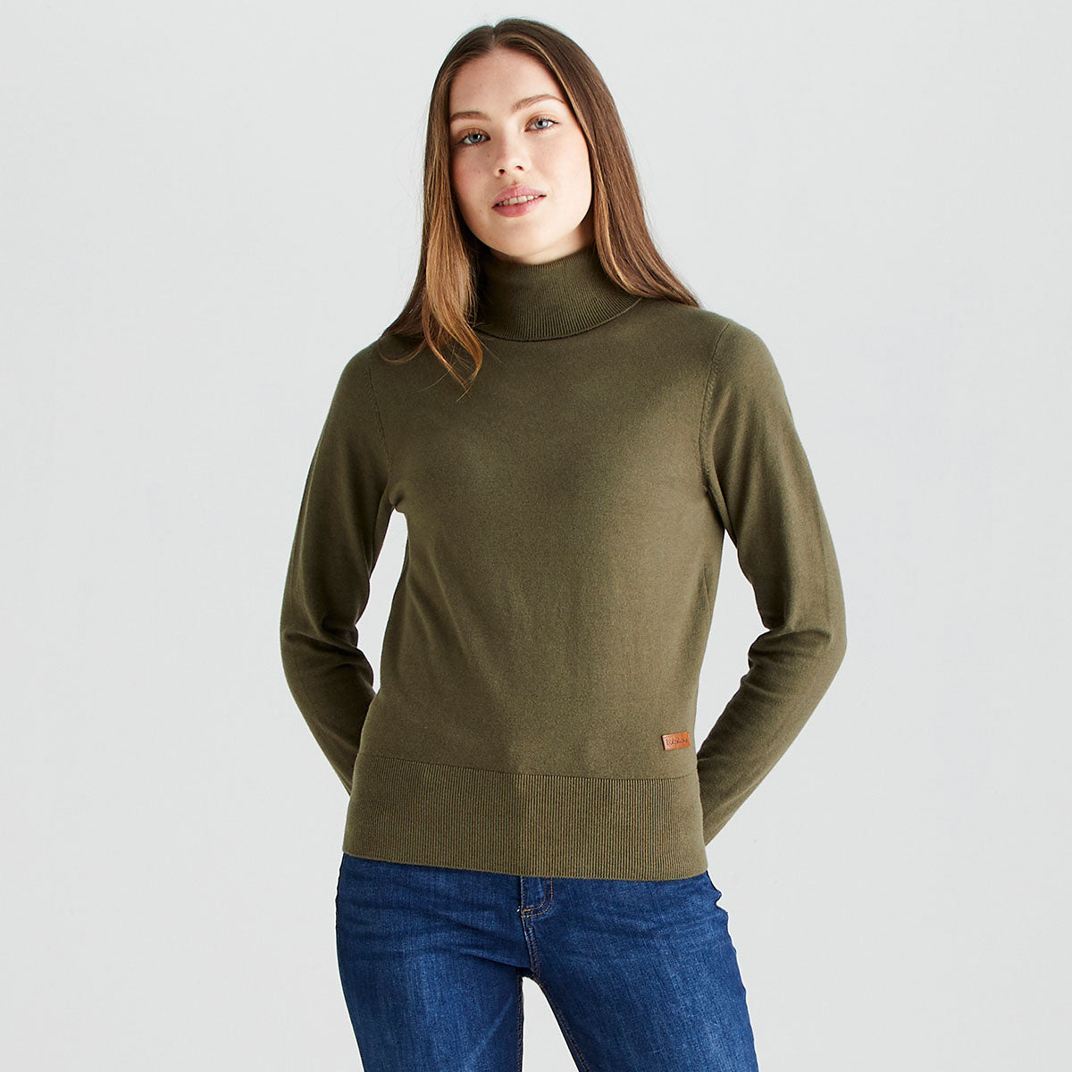 Front view of a model wearing a Ridgeline knitted roll neck pullover in olive green. The fine-knit jumper features a high roll-neck collar, long sleeves, and a ribbed hem, finished with a small Ridgeline logo tag near the waist. Styled with blue jeans against a light grey studio background.
