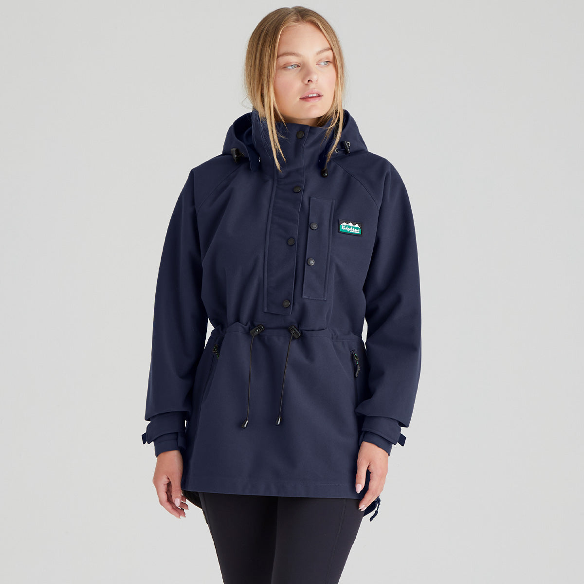 Woman wearing a navy blue waterproof jacket with a ridgeline clothing brand logo on a grey background