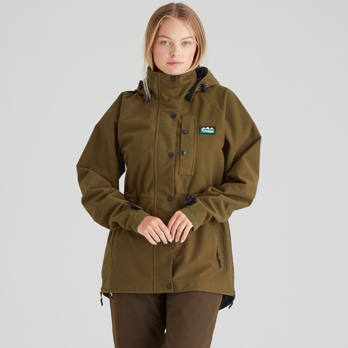 Person wearing a brown jacket with a visible brand logo on a grey background
