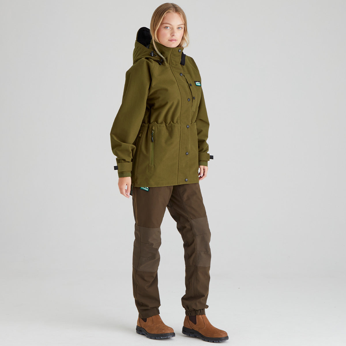 Person wearing a brown parka and brown pants on a light grey background