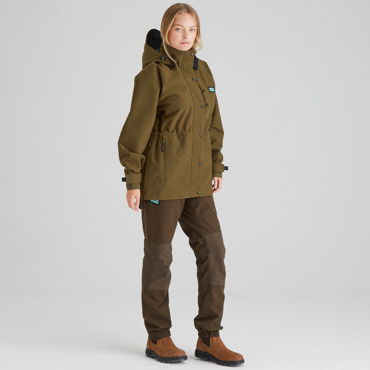 Person wearing a brown jacket and pants on a light grey background