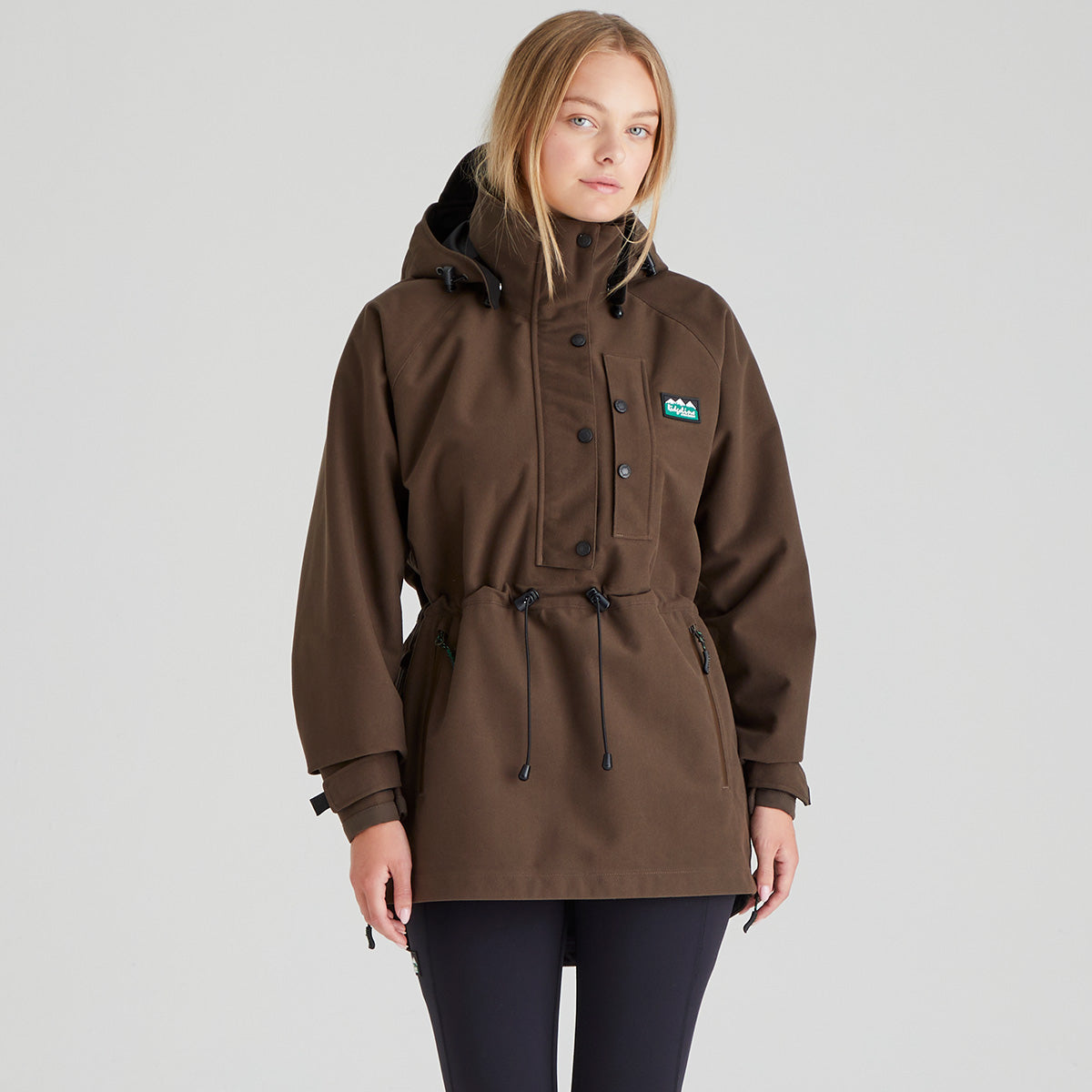 Woman wearing a brown waterproof jacket with a Ridgeline Clothing brand logo on a grey background