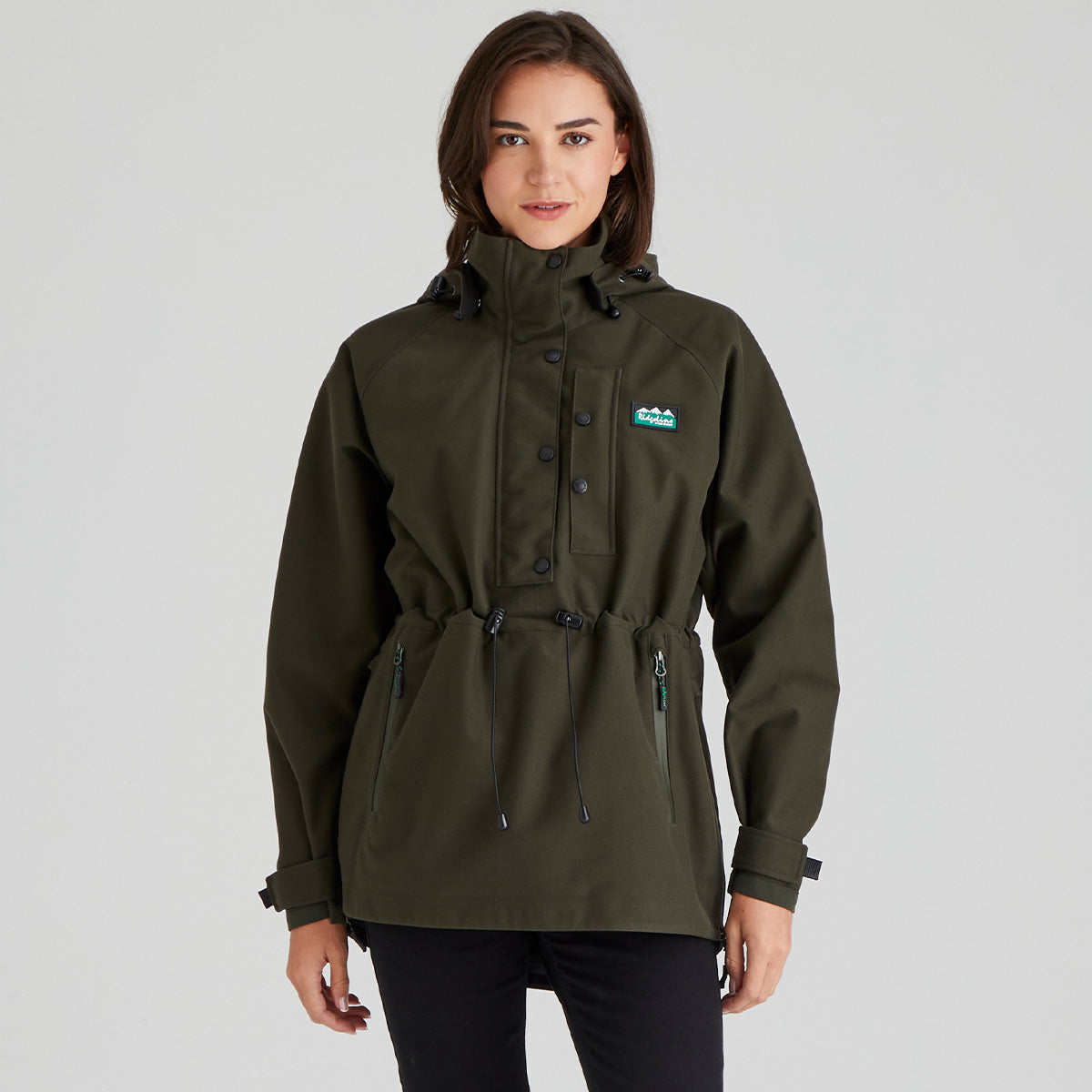 Person wearing a green waterproof  raincoat with a Ridgeline Clothing brand logo on a grey background