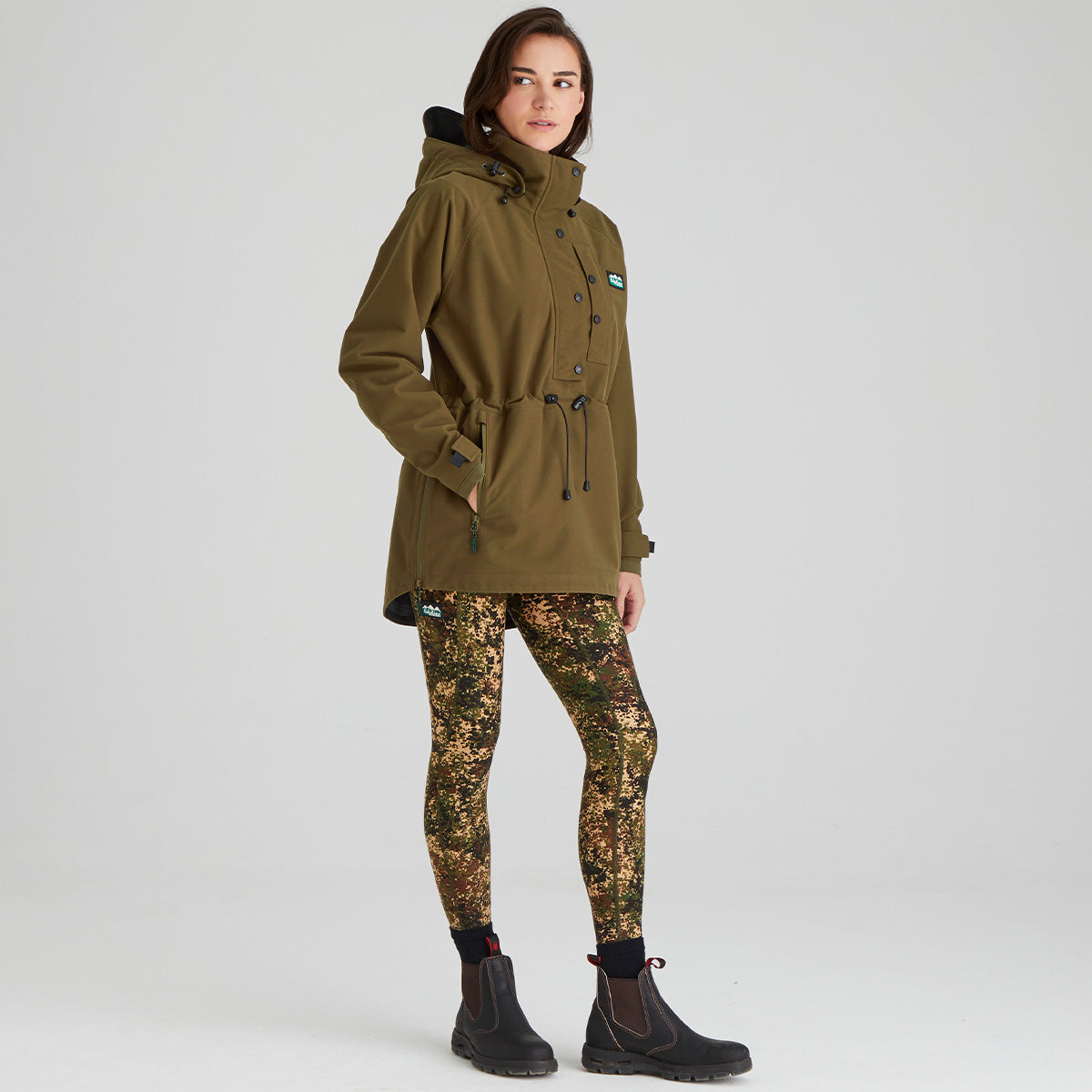 Person wearing a green/brown jacket and camouflage leggings on a white background