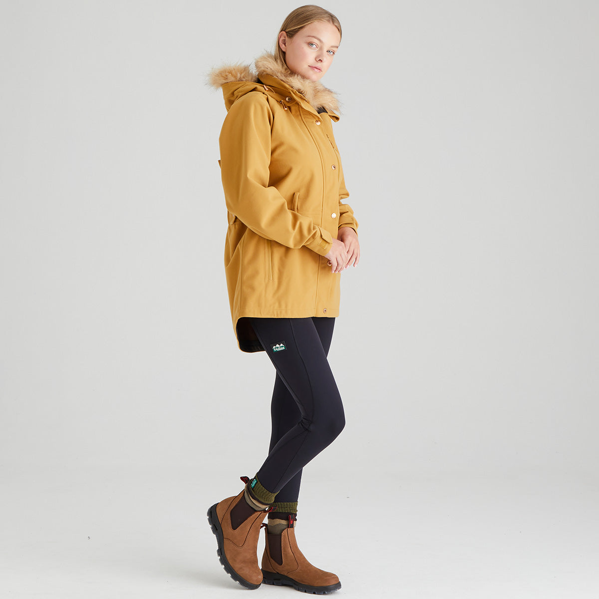 Woman wearing a mustard yellow parka with fur hood on a white background